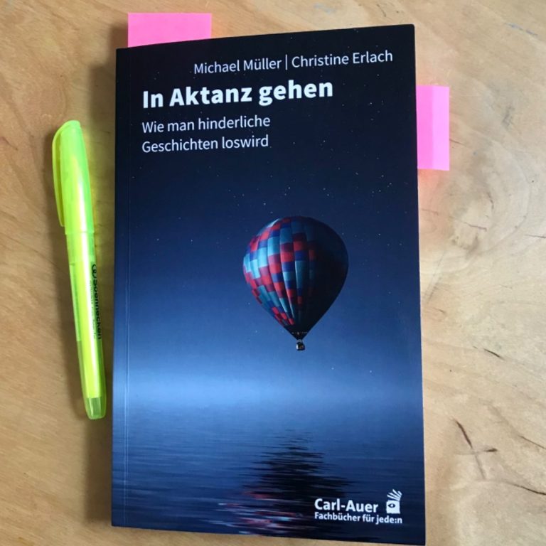 Buchcover eines Taschenbuchs mit dem Titel "In Altans gehen" auf Holztisch mit gelbem Textmarker daneben.